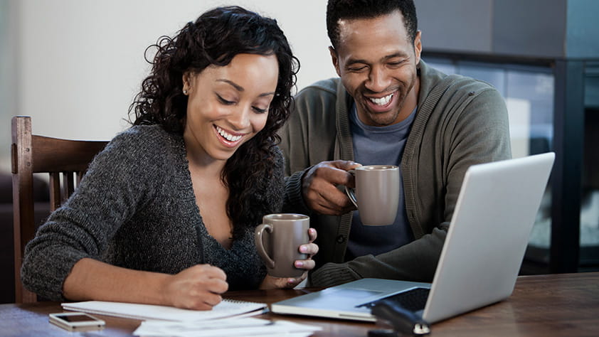 Couple working together on laptop with coffee and financial documents