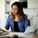 Woman reviewing financial documents at desk with laptop