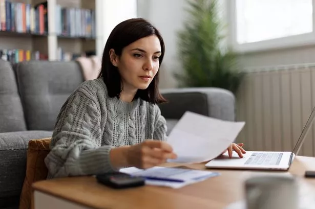 Woman reviewing financial documents with calculator and laptop