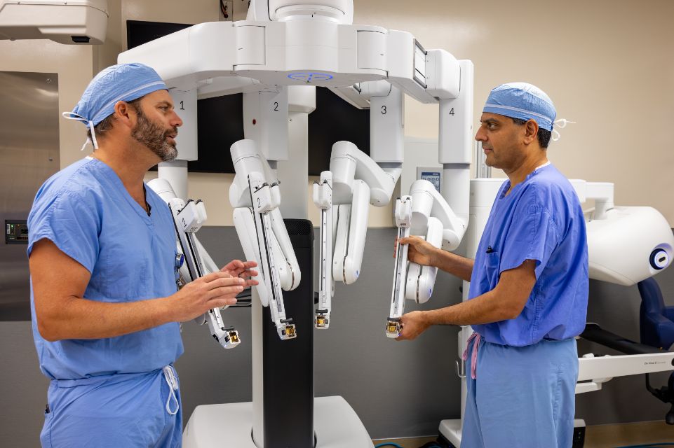 Two surgeons in blue scrubs examining da Vinci robotic surgical system arms