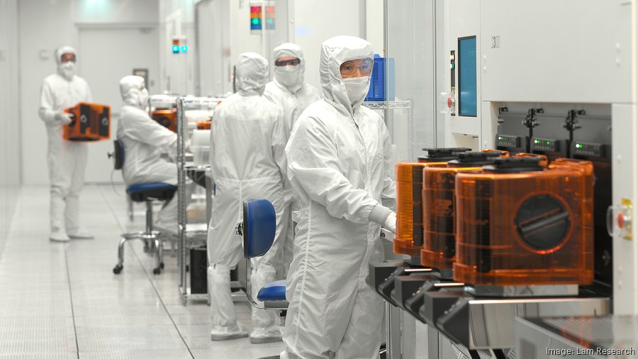 Semiconductor fabrication cleanroom with workers in protective suits handling wafer processing equipment