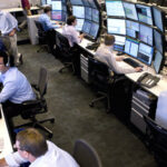 Professional traders working at multi-monitor trading desks in a modern proprietary trading office