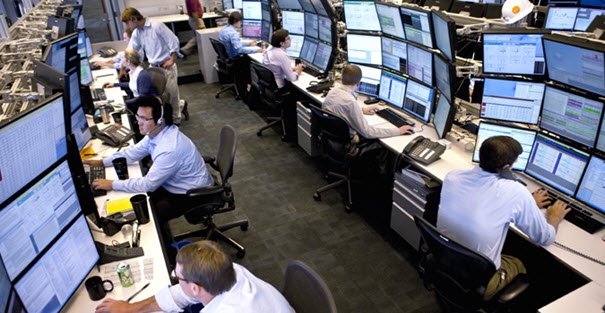 Professional traders working at multi-monitor trading desks in a modern proprietary trading office