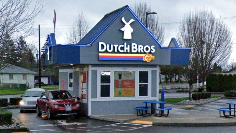 Dutch Bros drive-thru on an overcast day with illuminated signage and wet pavement, demonstrating the all-weather appeal of the drive-thru model