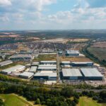 Aerial view of a large industrial and logistics estate with warehouses, surrounded by farmland and residential areas.