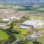Aerial view of a logistics business park with warehouses and surrounding development land and green fields.