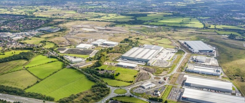 Aerial view of a logistics business park with warehouses and surrounding development land and green fields.