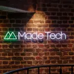 Illuminated Made Tech neon logo sign mounted on an exposed brick wall in the company's office