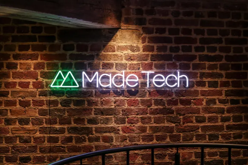 Illuminated Made Tech neon logo sign mounted on an exposed brick wall in the company's office