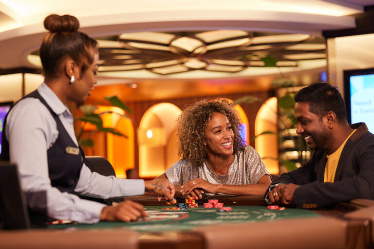 Casino dealer and two smiling customers at a blackjack table with chips, representing casino/gaming operations