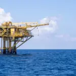 Yellow offshore oil and gas platform standing in open blue sea under a partly cloudy sky