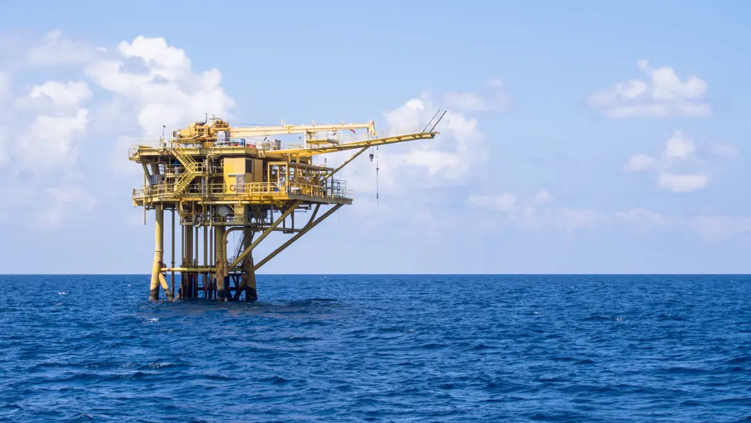 Yellow offshore oil and gas platform standing in open blue sea under a partly cloudy sky
