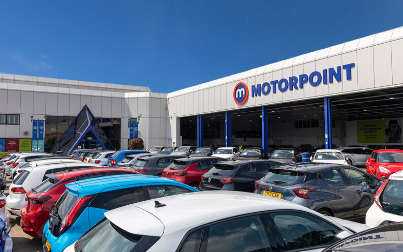 Exterior of a Motorpoint car dealership with a car park full of vehicles under a clear blue sky