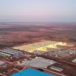 Aerial view of an illuminated data center and electrical substation facility in a rural landscape at dusk