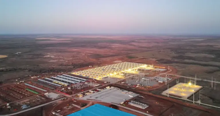 Aerial view of an illuminated data center and electrical substation facility in a rural landscape at dusk