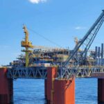Offshore oil platform standing on orange support pillars in open ocean under a clear sky