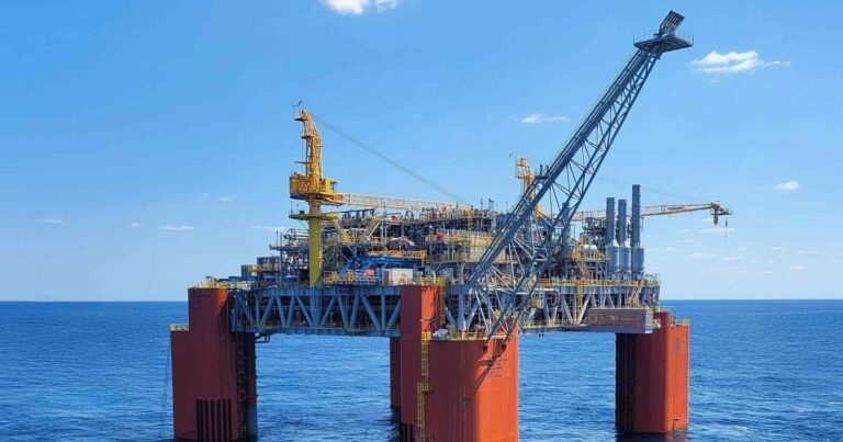 Offshore oil platform standing on orange support pillars in open ocean under a clear sky