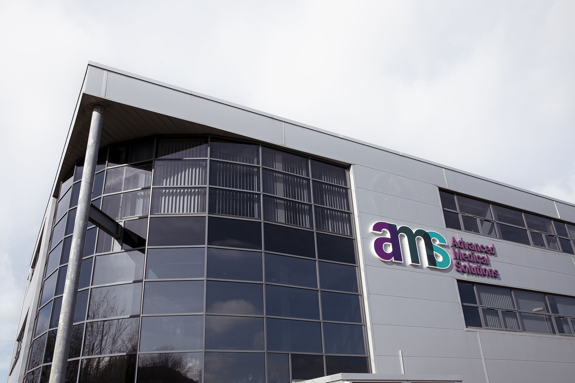 Exterior of Advanced Medical Solutions Group headquarters building with illuminated AMS logo and wordmark on the facade.