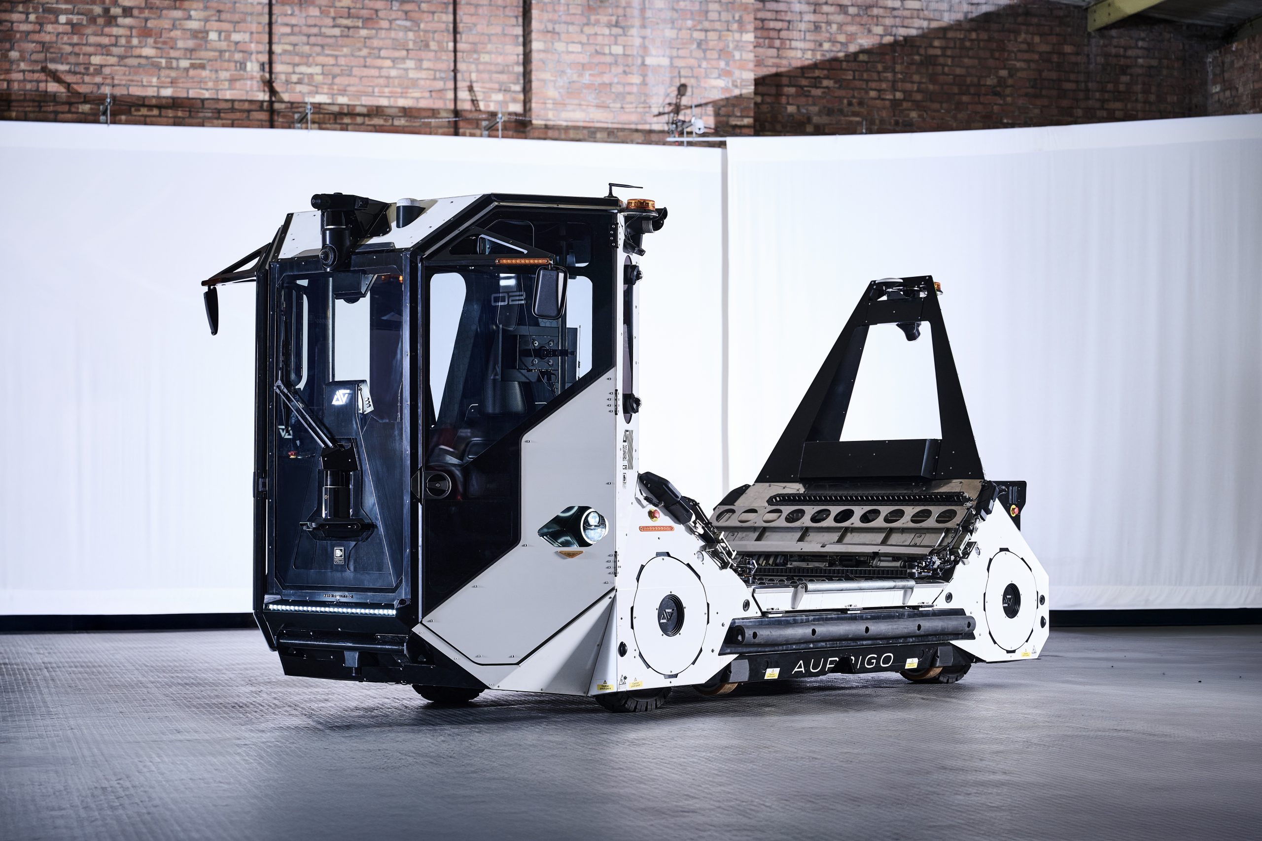 Aurrigo autonomous ground support vehicle with towing frame displayed in an industrial facility, branded with the Aurrigo name and logo.