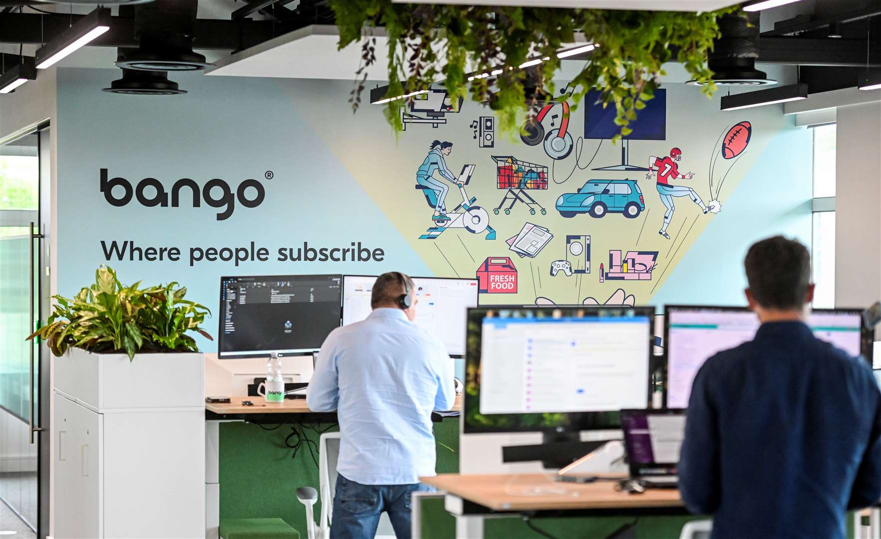 Employees working at desks in Bango plc's office, with the company logo and 'Where people subscribe' tagline displayed on the wall behind them.