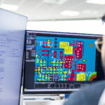 An engineer reviewing detailed printed circuit board design software on a computer monitor in an office environment, illustrating embedded electronics engineering work.