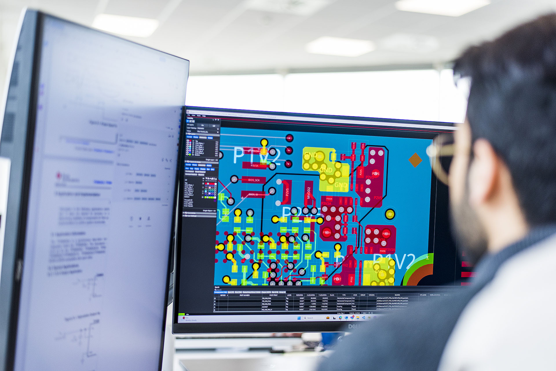 An engineer reviewing detailed printed circuit board design software on a computer monitor in an office environment, illustrating embedded electronics engineering work.