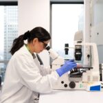 hVIVO scientist in a lab coat examining a sample under a microscope in a modern clinical research laboratory