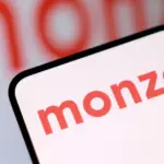 Smartphone displaying the Monzo logo, with a blurred Monzo wordmark visible in the background