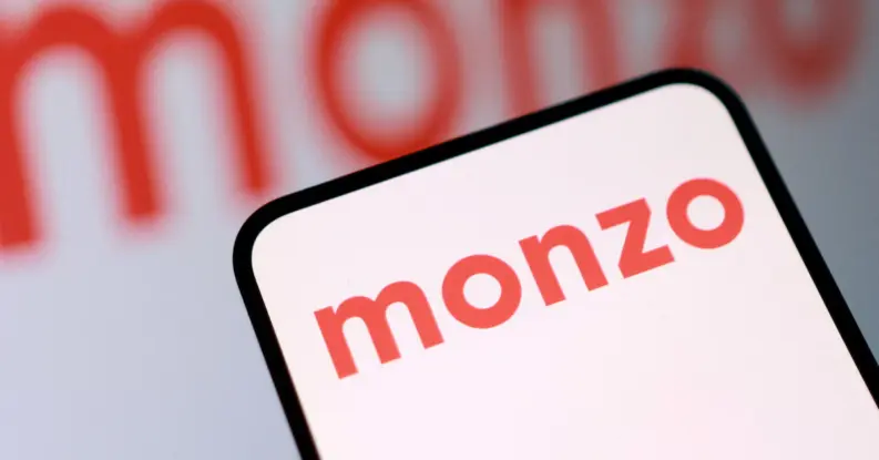 Smartphone displaying the Monzo logo, with a blurred Monzo wordmark visible in the background