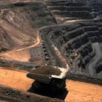 Aerial view of an open-pit mining operation with a loaded haul truck driving along a dirt road between excavated rock terraces