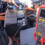 Technician using a Power Probe diagnostic multimeter to test a vehicle's electrical system under the hood