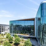 Aerial view of a modern glass office building with the Workday logo on its roofline, beside a landscaped courtyard and parking structure