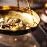 Raw gold nuggets piled on a brass weighing scale, symbolising precious metal value and commodity prices