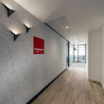 Modern office corridor with wood flooring and a red 'Bridgepoint Credit' wall sign, glass-walled meeting rooms visible in the background.