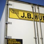 Close-up of a J.B. Hunt trailer door showing the company's yellow and black logo against a blue sky.