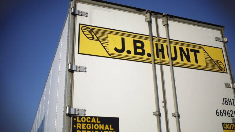 Close-up of a J.B. Hunt trailer door showing the company's yellow and black logo against a blue sky.