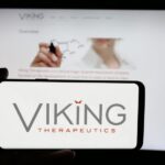 Smartphone displaying the Viking Therapeutics logo held in front of a blurred screen showing the company's website.