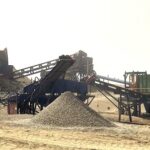 Heavy mineral sands mining and processing equipment including an excavator, conveyor, and mobile crusher at an open-pit site
