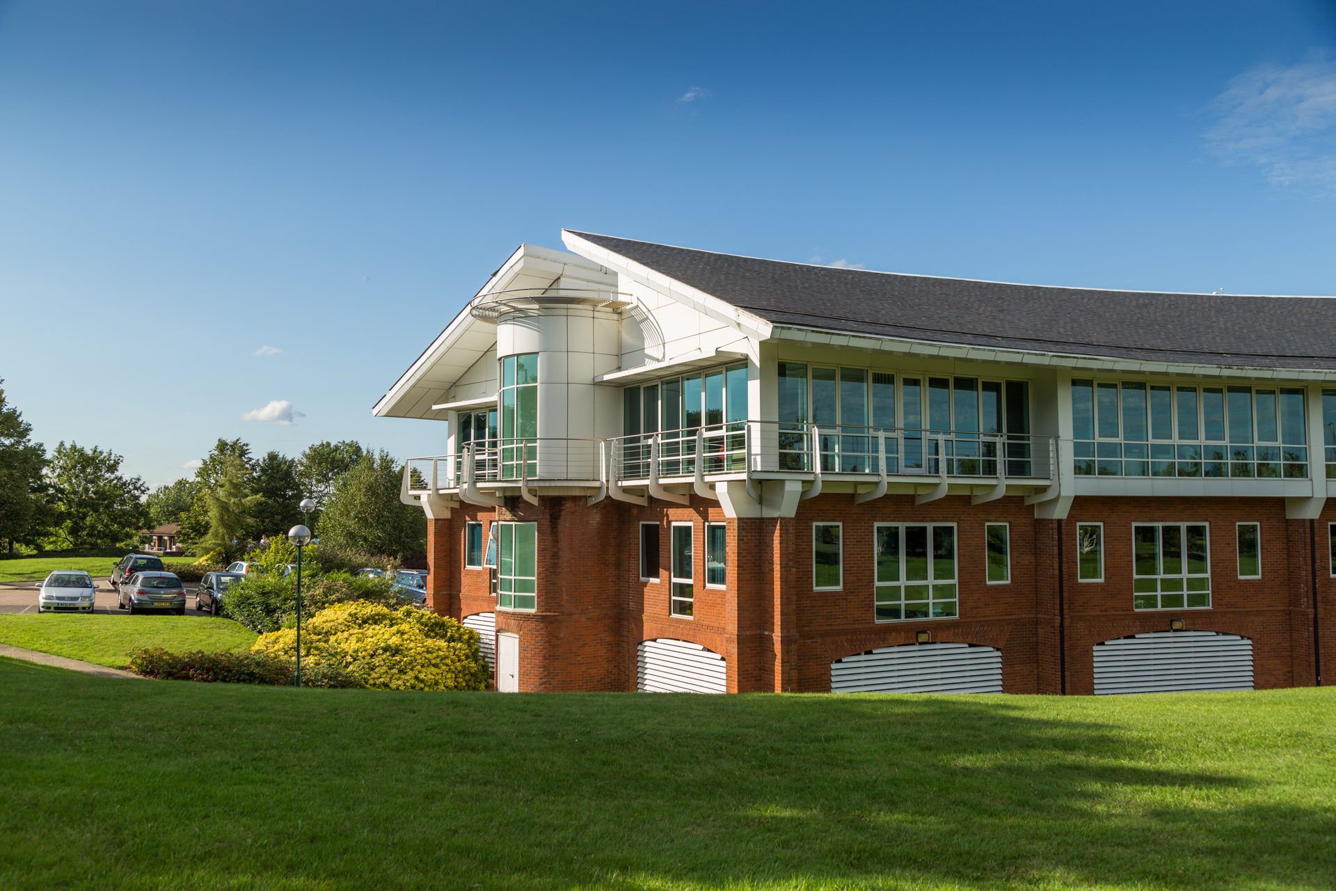 Exterior view of a modern corporate office building with brick and glass facade, set on a landscaped lawn under a clear sky
