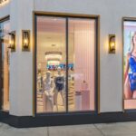 Modern Victoria's Secret storefront with illuminated display windows showing mannequins and a lingerie campaign poster.
