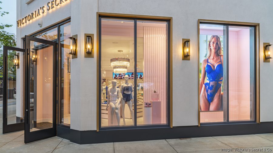 Modern Victoria's Secret storefront with illuminated display windows showing mannequins and a lingerie campaign poster.