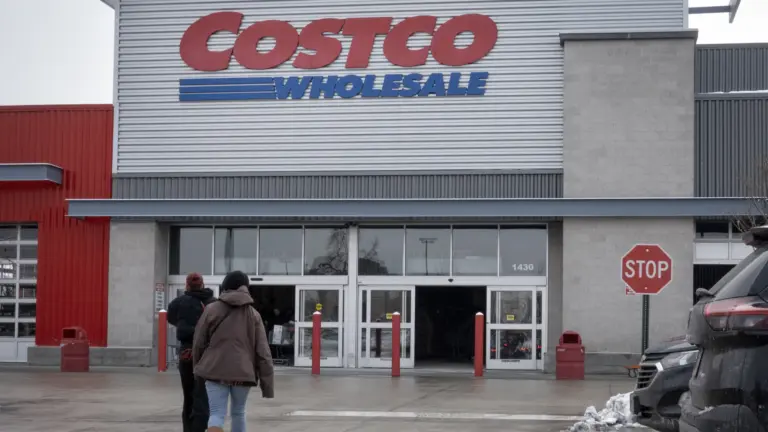 Exterior of a Costco Wholesale store with customers walking toward the entrance on a snowy day.
