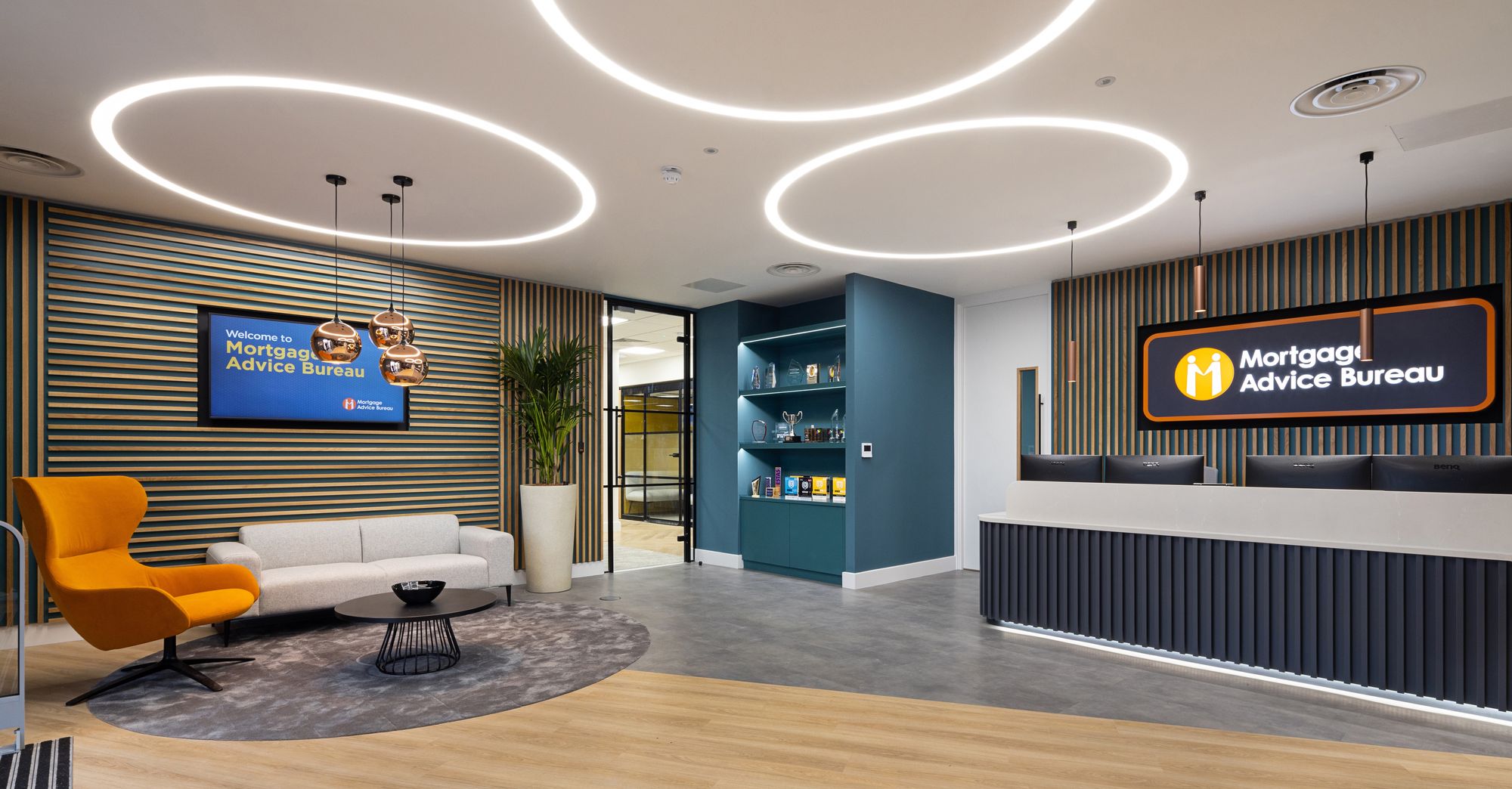 Modern reception area of a Mortgage Advice Bureau office with branded wall signage, a welcome screen, orange armchair, and wood-slat walls.