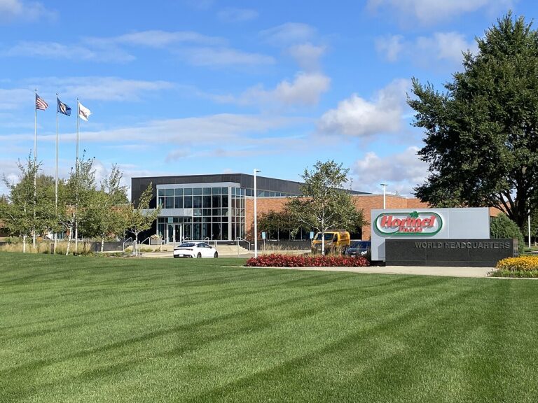 Hormel Foods world headquarters building with company sign and flags behind a mown lawn under a blue sky