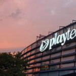 Playtech company logo illuminated on the exterior of its office building at sunset.