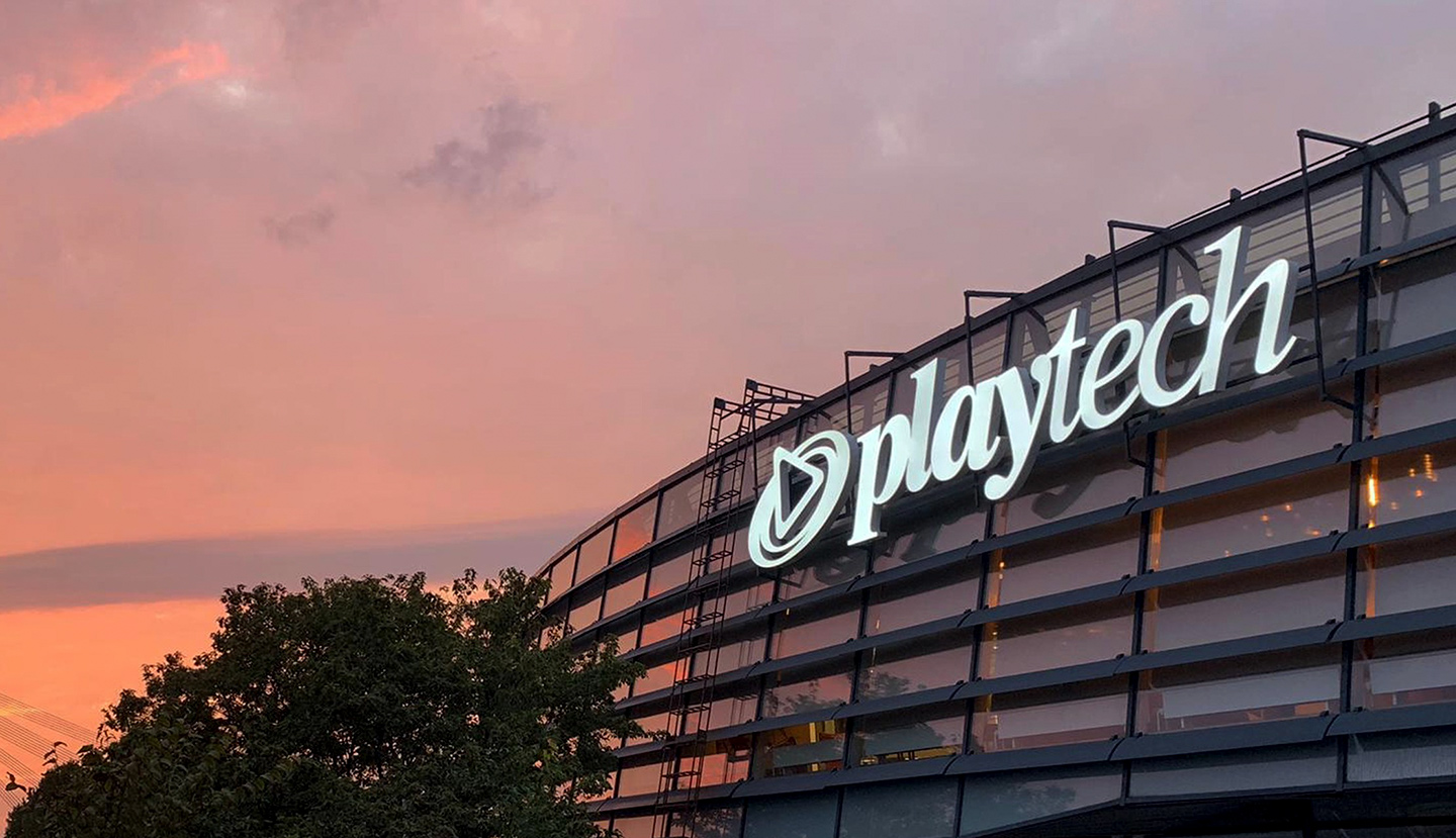 Playtech company logo illuminated on the exterior of its office building at sunset.