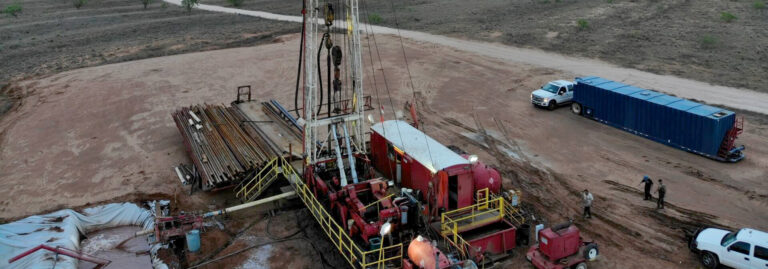 Aerial view of an active oil drilling rig site with equipment, vehicles, and workers on open land