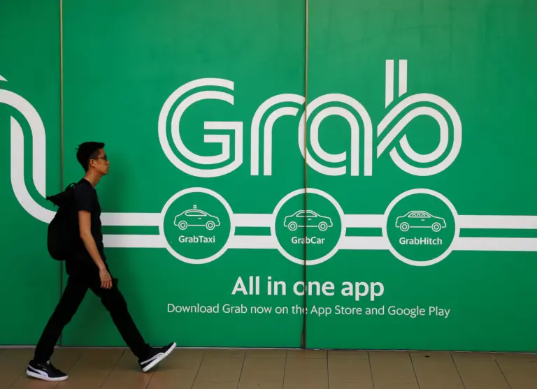 A pedestrian walks past a large green Grab advertisement billboard promoting GrabTaxi, GrabCar, and GrabHitch services.