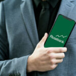 Businessman holding a smartphone displaying the Rosebank logo and an upward stock chart