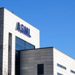 Blue ASML lettering on the corner of a modern light-coloured office building against a clear blue sky